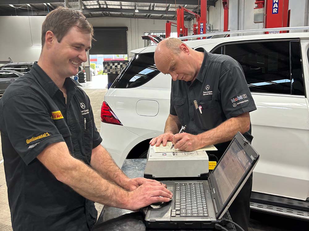 2 mechanics at a desk in front of a car